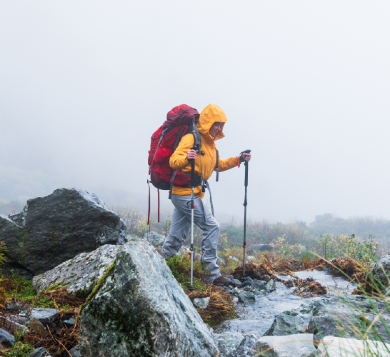 A person hiking with a red backpack and trekking poles in the fog.