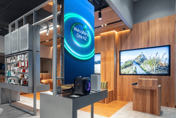 Interior of a One NZ retail store featuring a large digital "Welcome to One NZ" screen and sleek wooden and metal product displays.