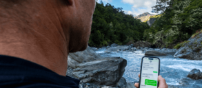 Person near a river holding a smartphone showing a messaging app.