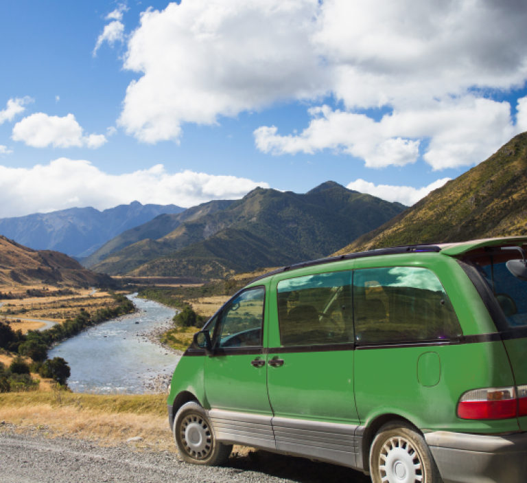 A green van parked on the side of the road with beautiful landscape on the background.