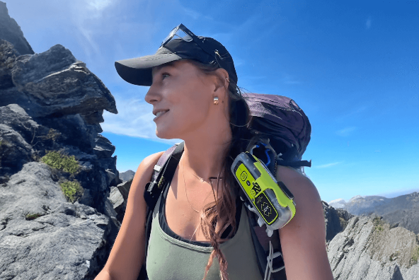 A woman hiking on a rocky mountain trail with a large backpack under clear blue skies.