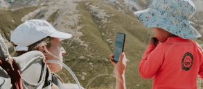 A mother looking at a phone with her child standing next to her.