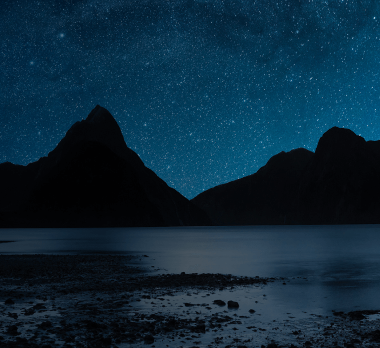 A night view of the stars and satellites, reflected over a lake.