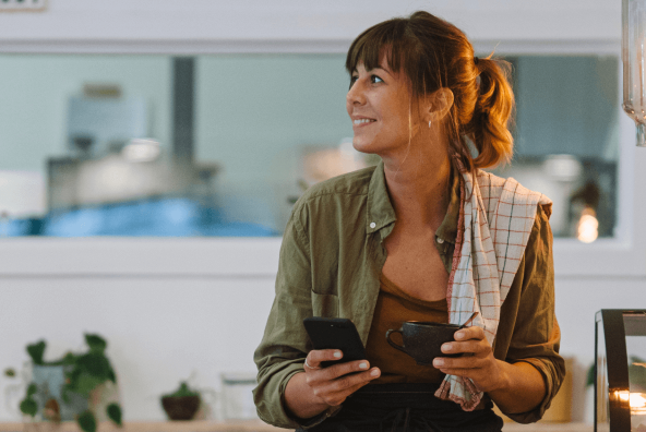 Lady working at a cafe holding phone on one hand and a coffee cup on other.