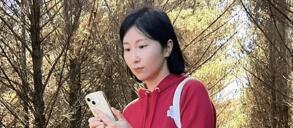 Person in a red hoodie holding a smartphone in a forest.