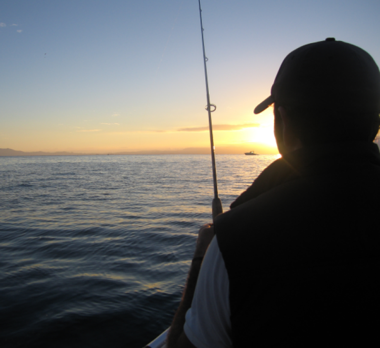 A person fishing at sunset on a calm sea.