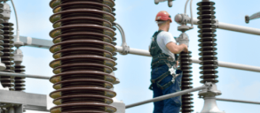 Worker in safety gear inspecting electrical equipment at a power substation.
