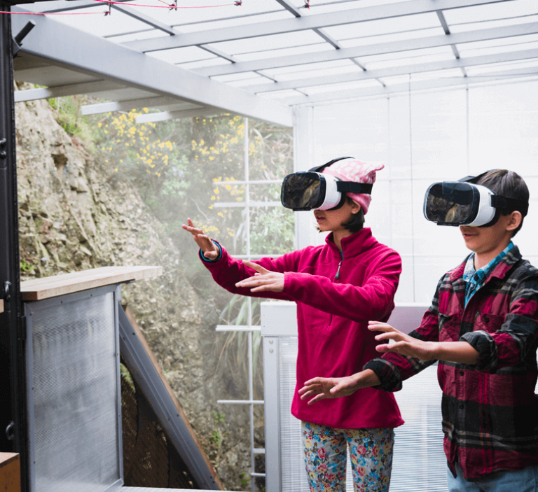 Brother and sister using virtual reality goggles on veranda.