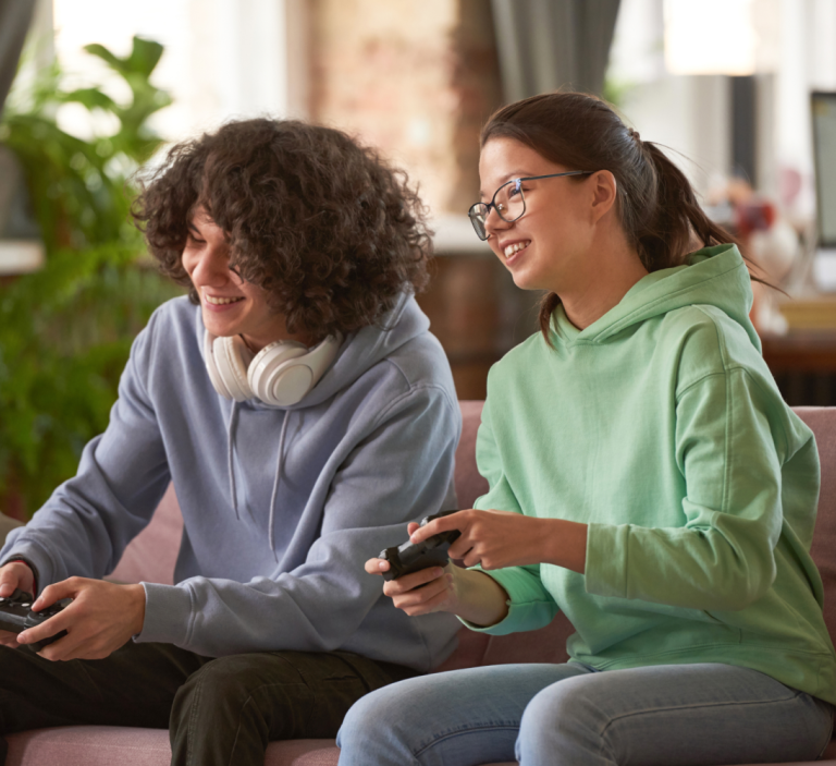 Two teenagers sitting on a couch playing video games.
