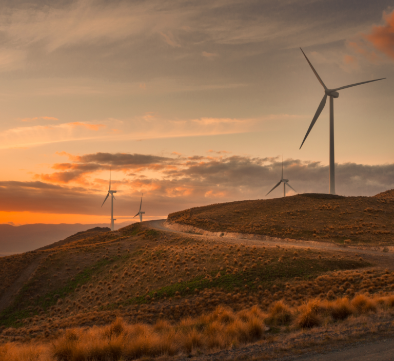 Wind turbines on a hill with the sun setting over the horizon.