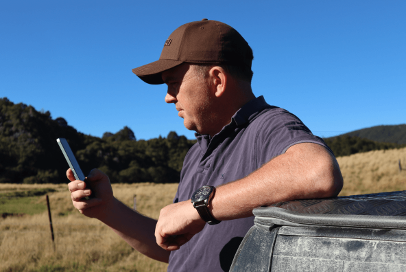 A man holding a phone and leaning on a vehicle in a field.