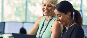 Two women colleagues smiling, looking and pointing at a laptop.